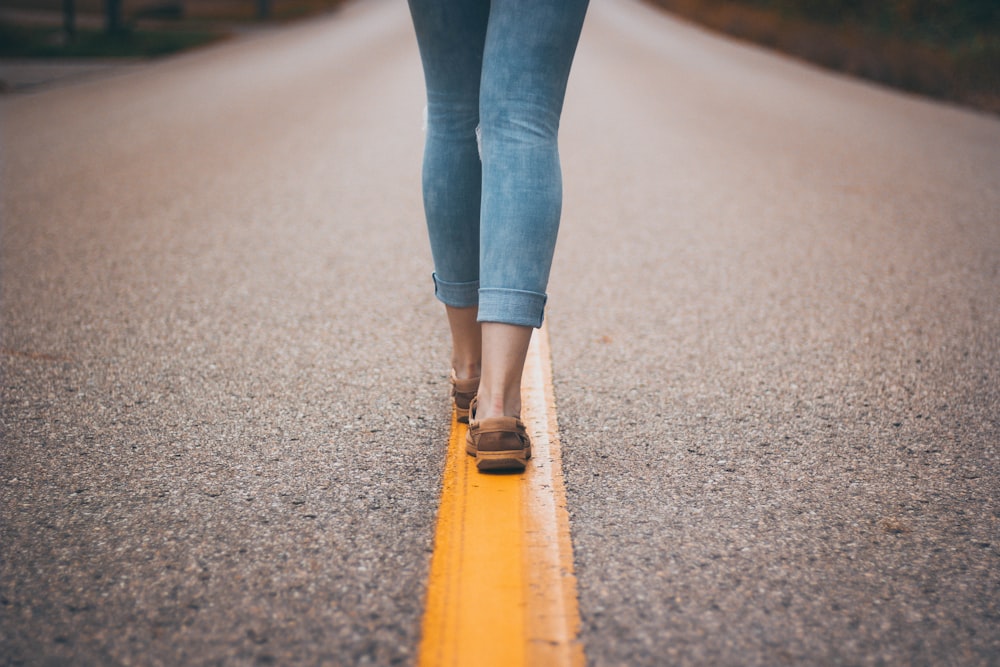 pessoa usando sapatos marrons em pé na estrada da linha amarela durante o dia
