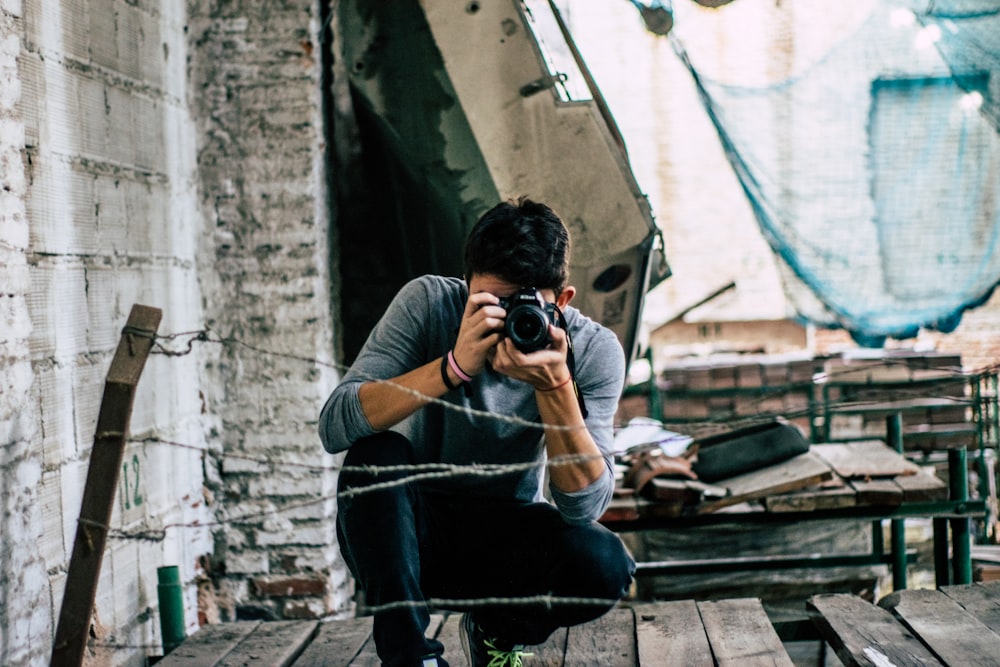 selective focus photography of man holding DSLR camera taking picture in front of barbwire