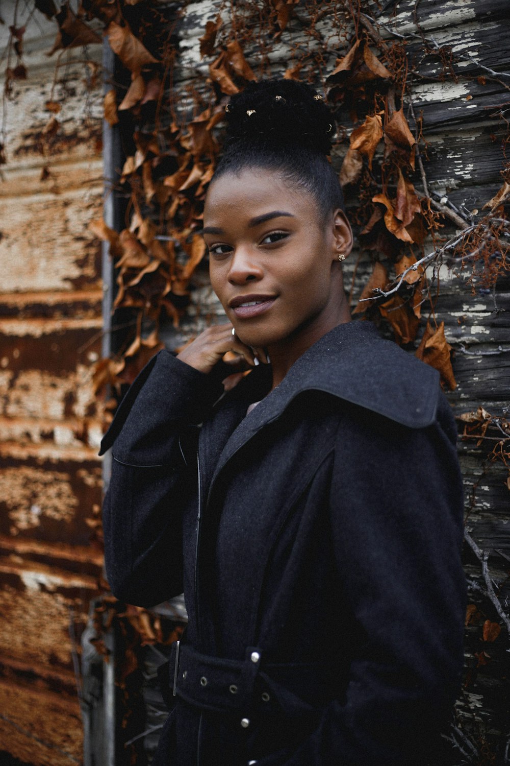 femme portant un manteau noir debout près de feuilles séchées