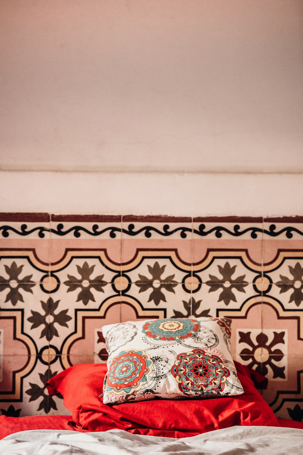 white, red, and blue mandala floral throw pillow placed on red pillowcase