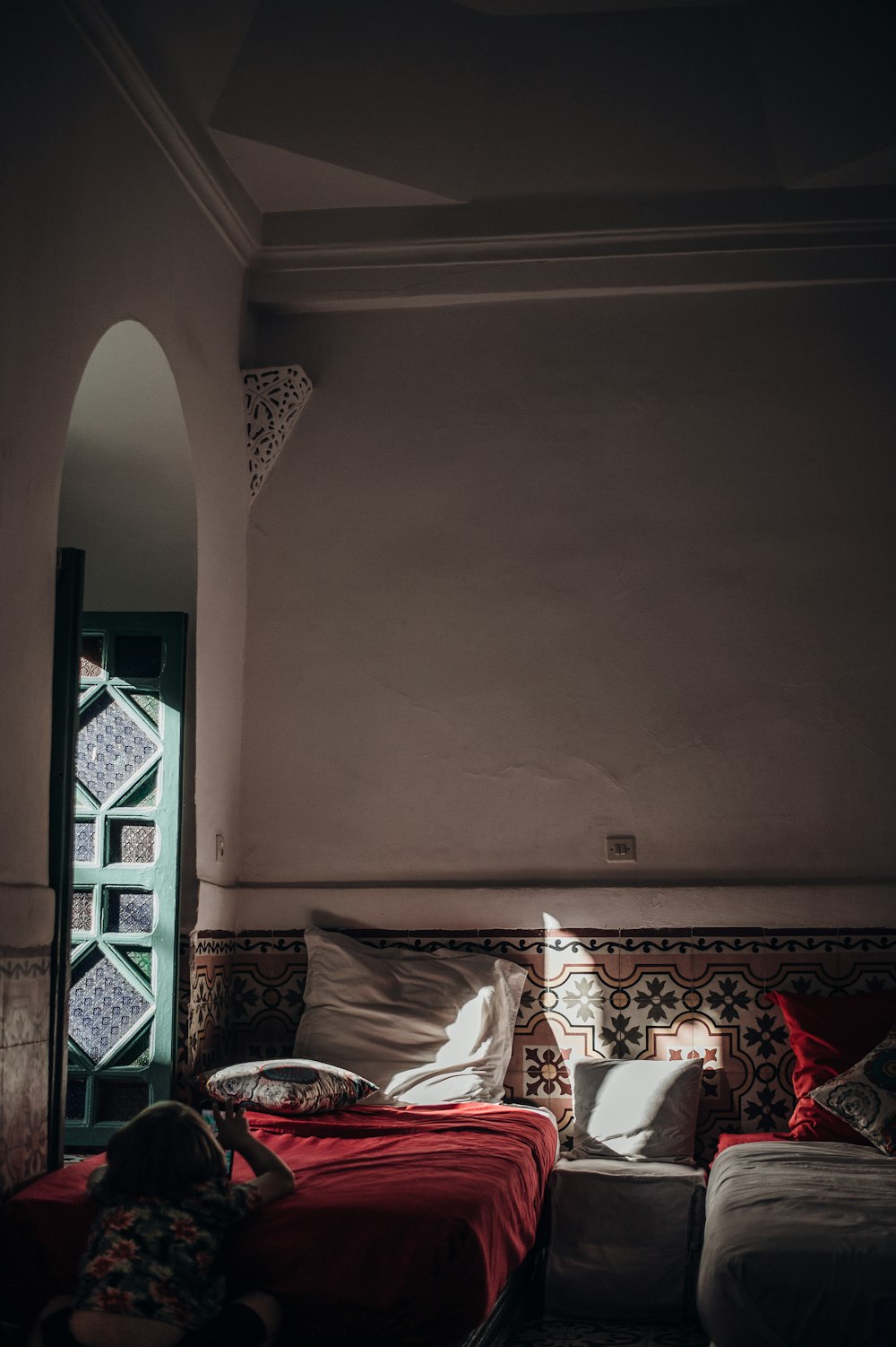 girl with smartphone sitting on floor facing bed inside white-painted room