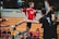 A smiling young male handball player in mid-action, wearing a Martinent Handball jersey on an indoor court.