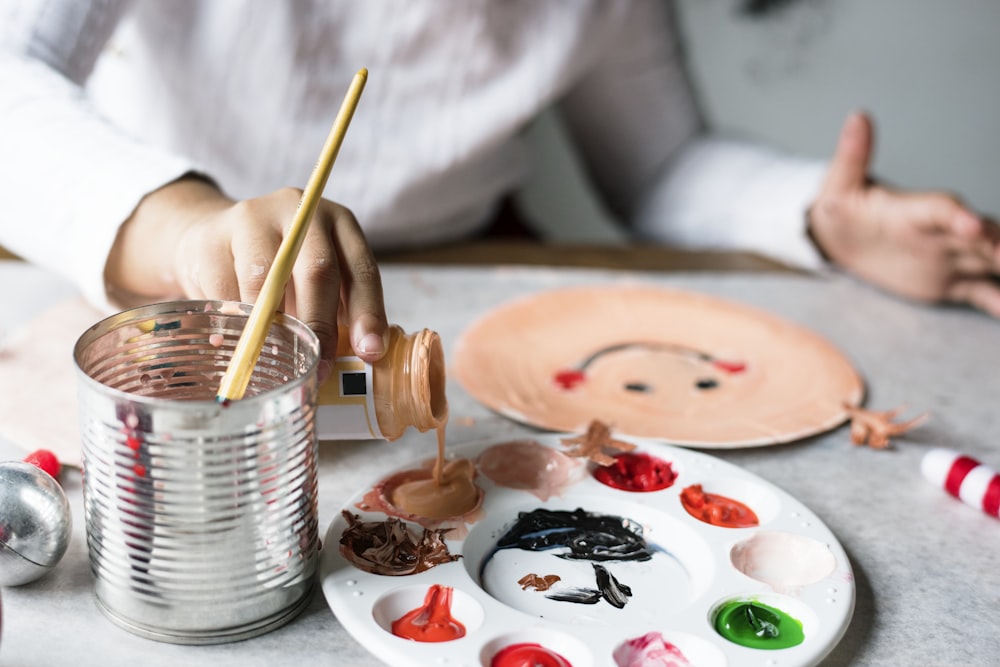 person pouring acrylic paint near can and paper