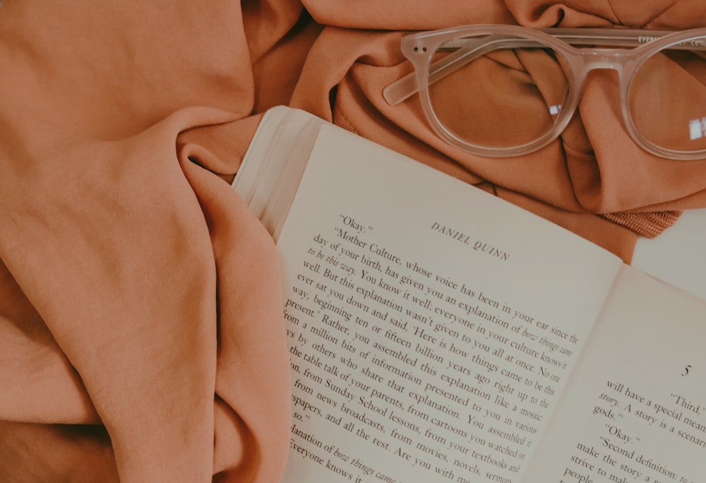 안경 근처의 분홍색 매트 위에 열린 책 페이지