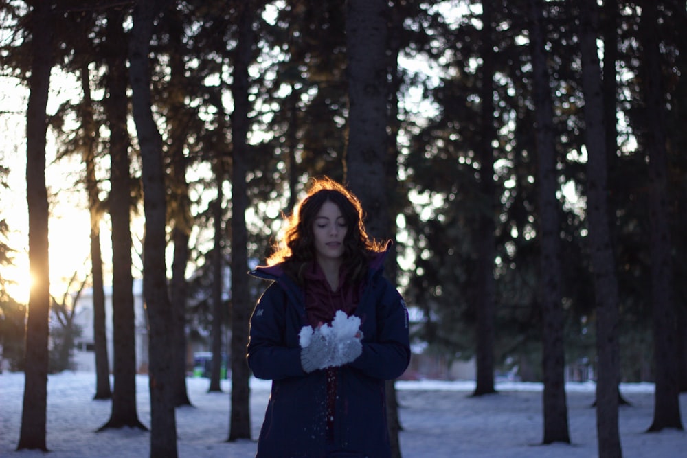 woman holding snow near trees during sunset