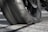 A close-up view of a worn motorcycle tire on a textured asphalt surface. The rubber appears smooth and the tread is nearly flattened, indicating significant use.