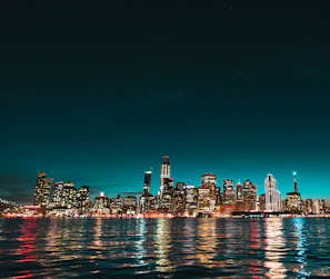 A futuristic cityscape at night with glowing turquoise lights under a dark blue sky