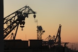 silhouette of metal cranes at worksite during golden hour
