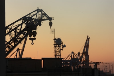 silhouette of metal cranes at worksite during golden hour