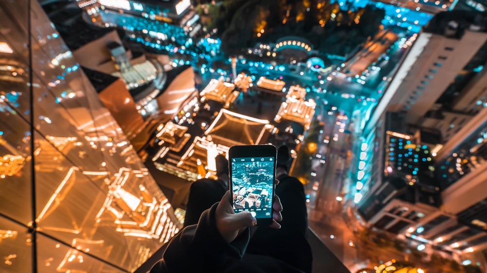 personne sur gratte-ciel prenant une photo du bâtiment ci-dessous pendant la nuit