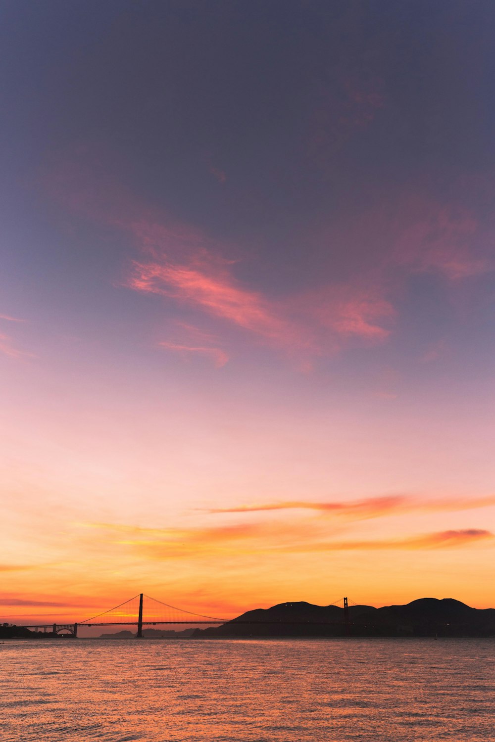 Silhouettenfotografie des Berges neben der Hängebrücke während der goldenen Stunde