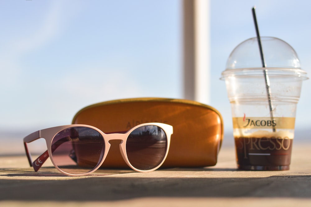 selective focus photography of white sunglasses near brown leather pouch and clear Jacobs Espresso disposable solo cup