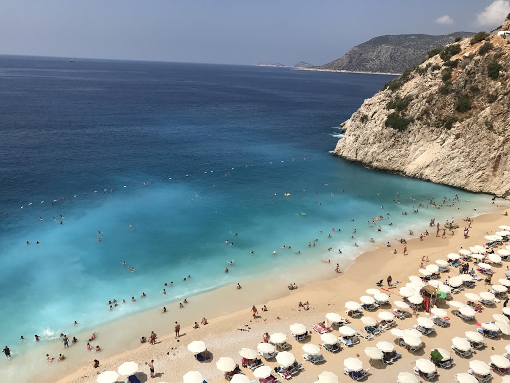 high angle photo of people gathering on seashore near mountain cliff