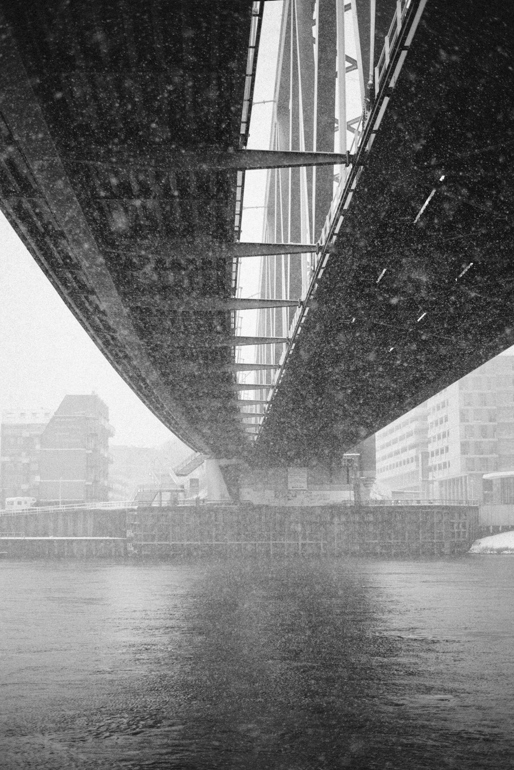 fotografia architettonica in scala di grigi del ponte metallico sottostante