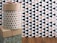 A patterned cylindrical box with a lid, adorned with red and silver polka dots, is stacked on a square box with a kraft paper appearance. A red and white string is placed on top. The background features a geometric black and beige triangle pattern on the wall, with a wooden floor beneath.