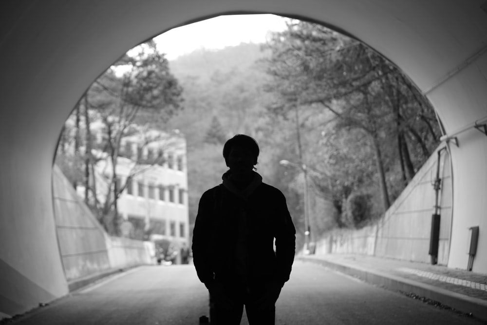grayscale photography of man standing in tunnel