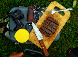 Close-up of a beautifully crafted oak chopping board alongside handmade BBQ tools on a rustic wooden table.
