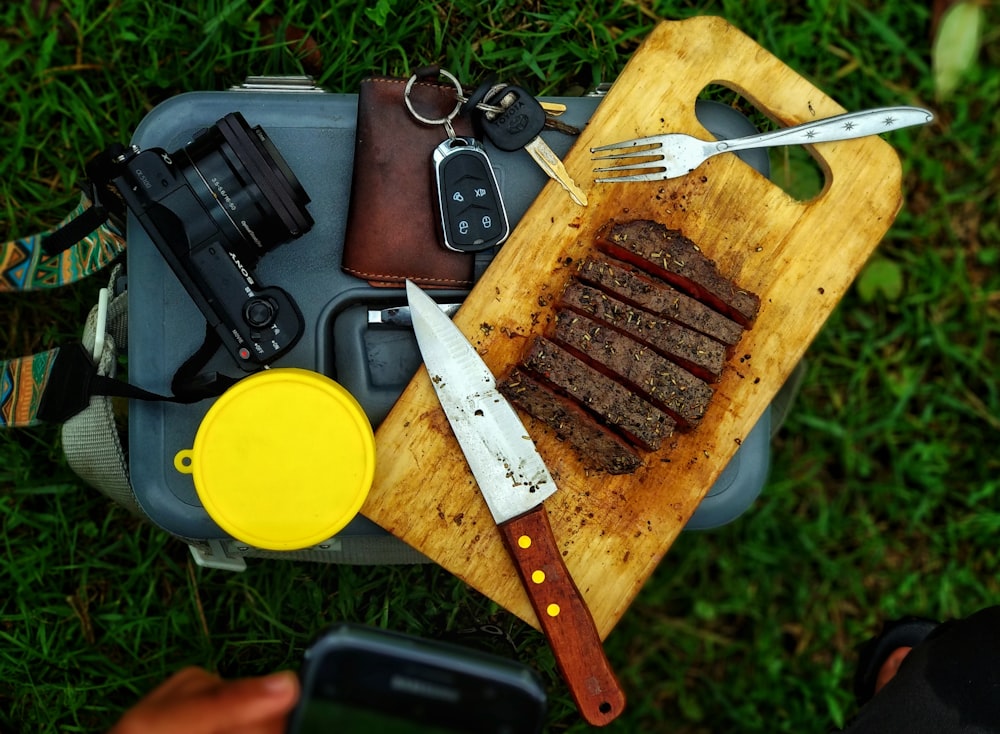 carne en rodajas en una tabla de cortar marrón junto a una cámara DSLR negra