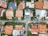 An aerial view of a residential neighborhood with neat rows of houses featuring a variety of roof colors and designs. Each house is surrounded by greenery, with well-maintained gardens and various trees. The layout forms a grid with roads separating the properties, and several vehicles are parked along the streets. The image captures a mix of traditional and modern architectural styles in a suburban setting.