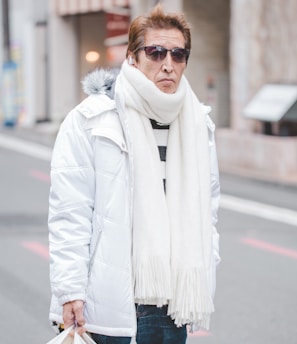man in white parka jacket and white scarf walking on street at daytime