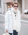 man in white parka jacket and white scarf walking on street at daytime