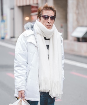 man in white parka jacket and white scarf walking on street at daytime