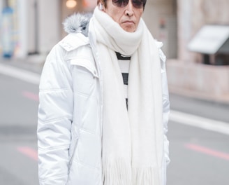 man in white parka jacket and white scarf walking on street at daytime