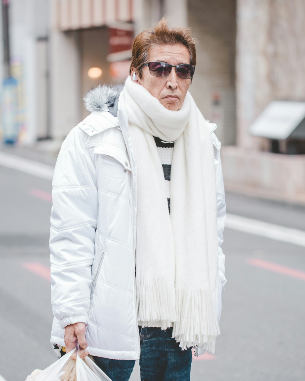 man in white parka jacket and white scarf walking on street at daytime