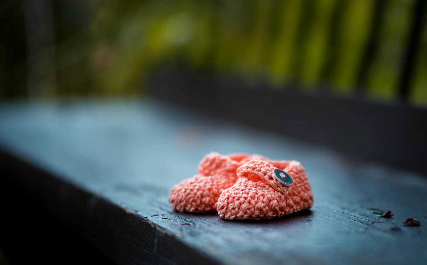 A pair of Strandby slippers in pink wool felt standing on a bench