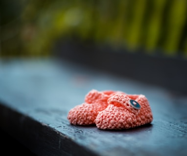 pair of baby's pink knit shoes on bench