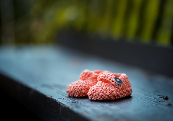 pair of baby's pink knit shoes on bench