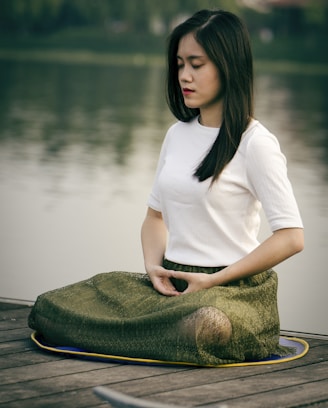 woman meditating on wooden dock during daytime