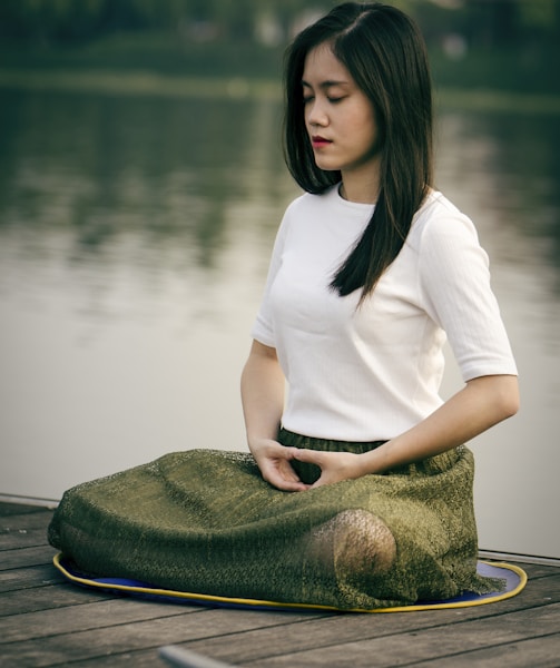 woman meditating on wooden dock during daytime