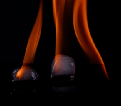Two ice cubes are placed on a reflective surface with orange flames rising above each cube against a dark background.