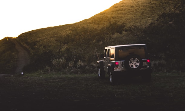A rugged 4x4 jeep parked on a mountain trail with the early morning sun casting golden light over Mount Batur.