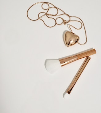 gold heart pendant necklace and two gold handled makeup brushes