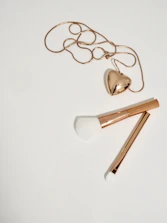gold heart pendant necklace and two gold handled makeup brushes