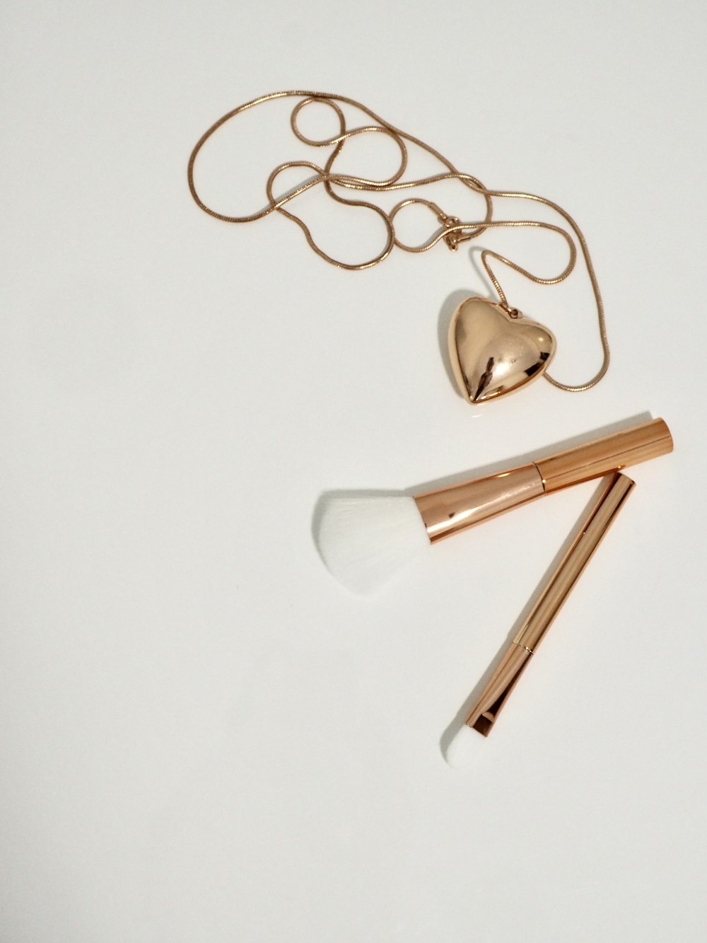 gold heart pendant necklace and two gold handled makeup brushes