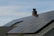 A house roof is covered with a large array of solar panels. The panels are angled to capture sunlight effectively and are bordered by a typical shingle roof. A red brick chimney protrudes through the center, indicating the presence of a fireplace or heating system inside.