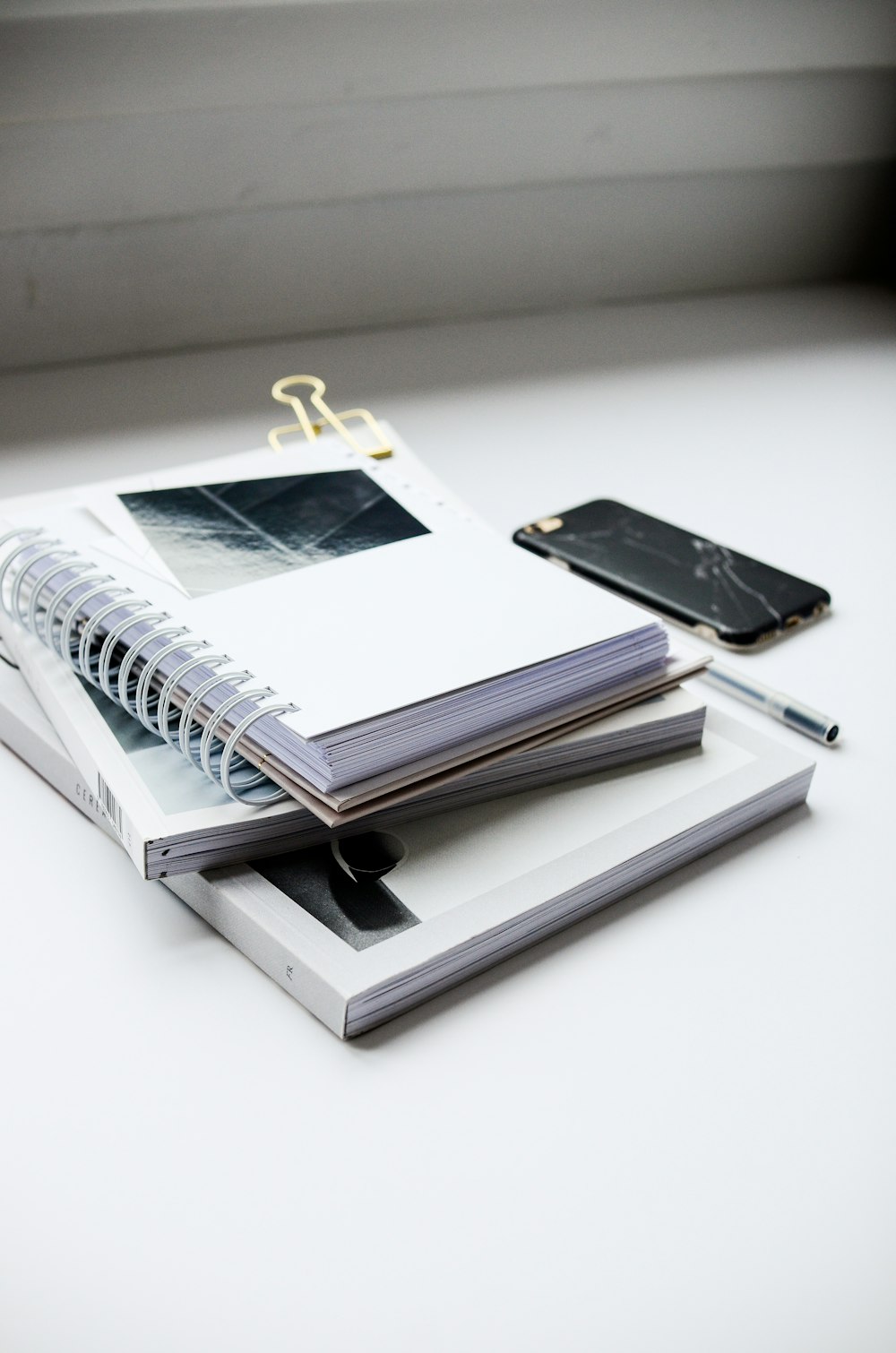 white spiral notebook beside black smartphone on white table