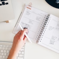 person holding notepad and pen flat lay photography