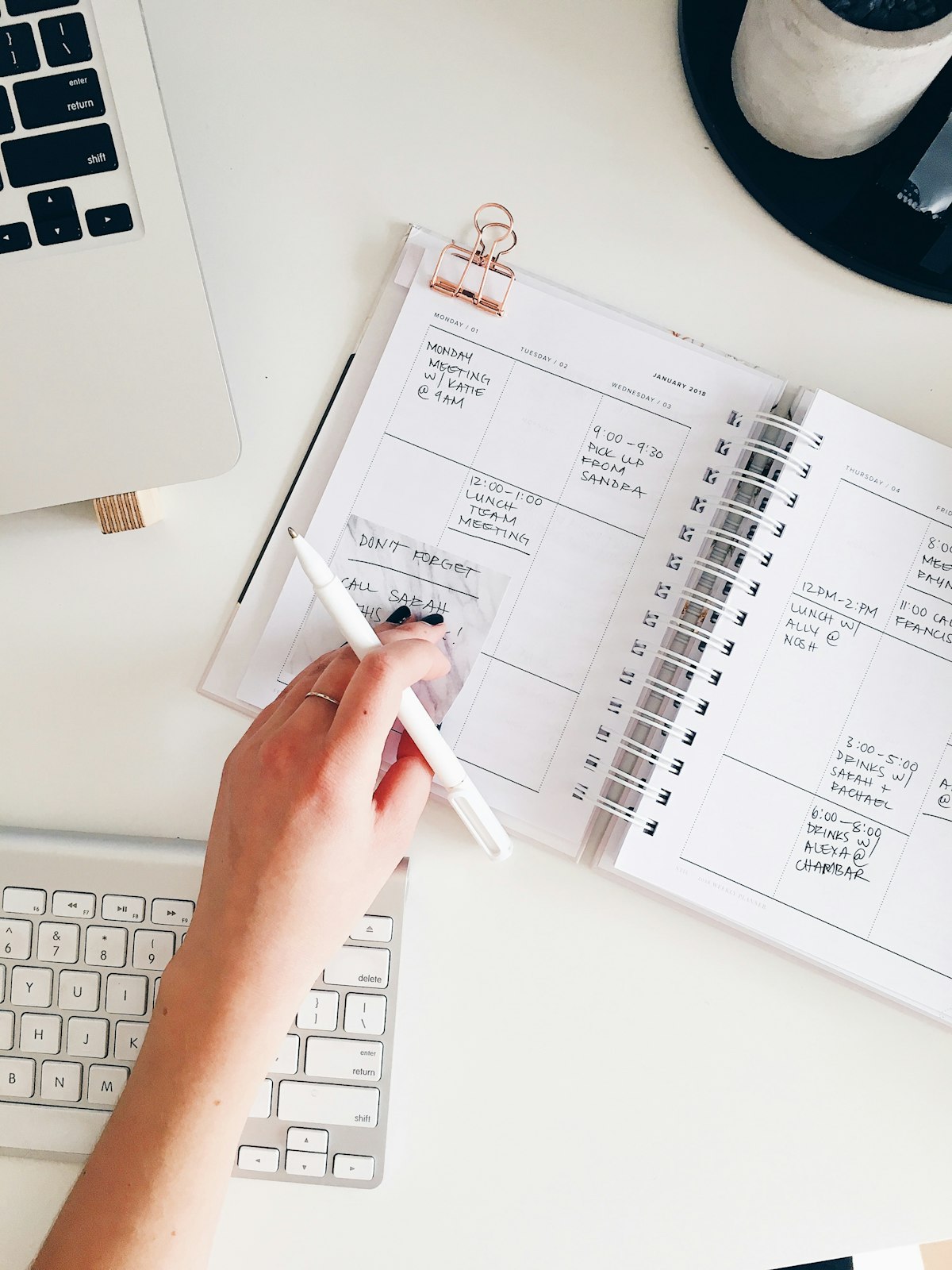 Hand writing in a planner with a keyboard nearby, signifying meticulous time management for busy professionals.
