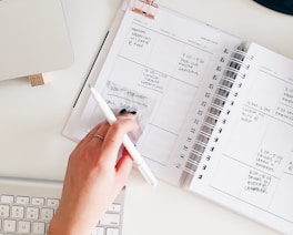 person holding notepad and pen flat lay photography