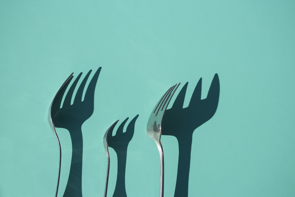 three gray metal forks casting shadow on green surface