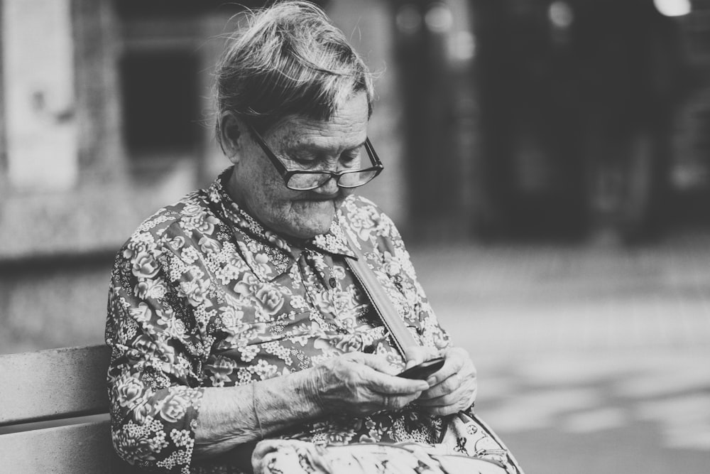 selective focus grayscale photography of woman using phone while sitting at bench