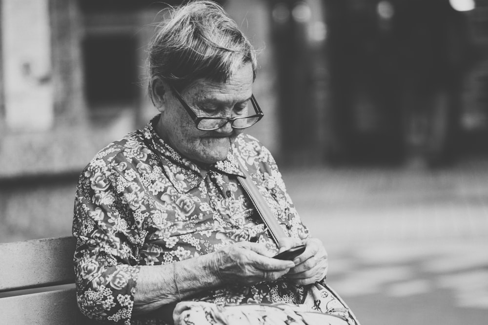 Fotografía en escala de grises de enfoque selectivo de mujer usando el teléfono mientras está sentada en el banco