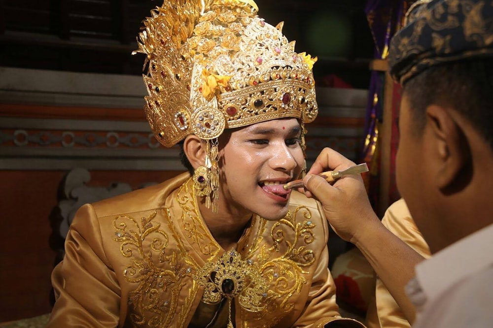 man wearing gold head dress opening his mouth