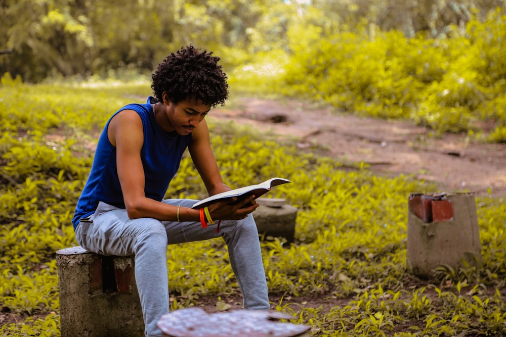 uomo che indossa una camicia blu seduto sulla panchina che legge il libro