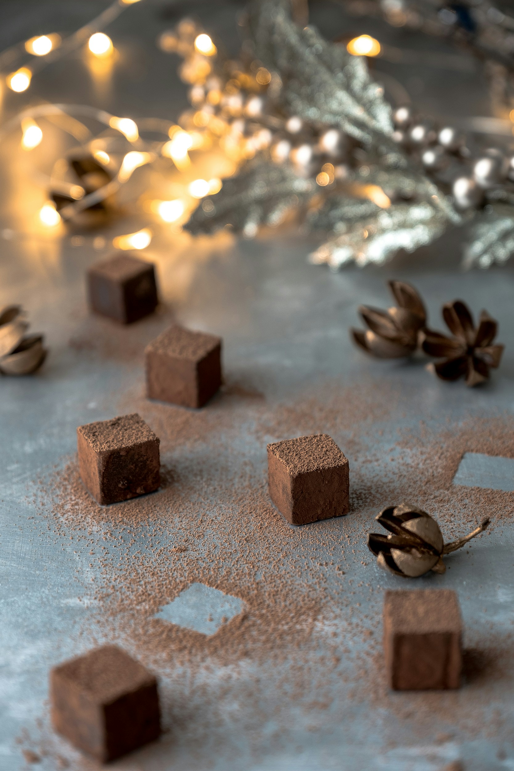 Dark chocolate truffles with cocoa dusting on black slate, dramatic side lighting, deep shadows