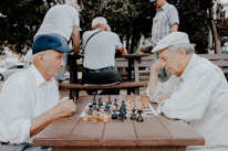 Two friends smiling and playing chess on a tablet in a park.